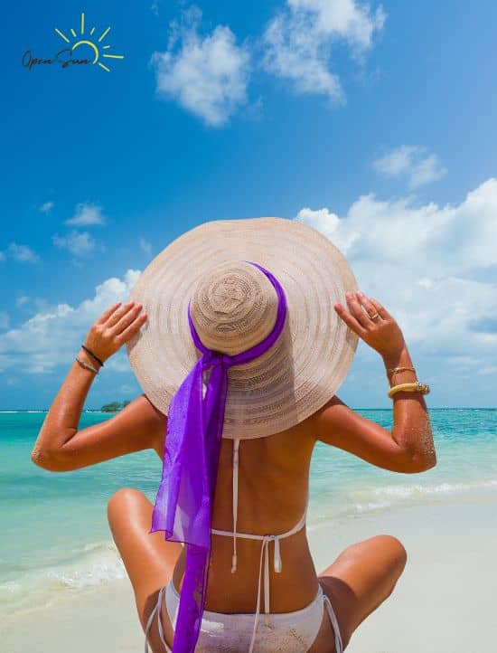 femme de dos sur une plage en maillot de bain au soleil avec un chapeau 